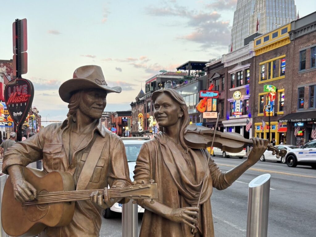 ブロードウェイ通りにあるカントリーミュージシャンの銅像と背景のネオン街