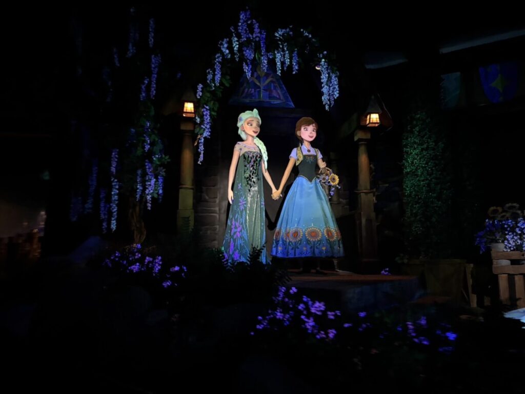 エプコットの「フローズン・エバー・アフター」で登場するアナとエルサ。暗い室内で手をつないで立つシーン。