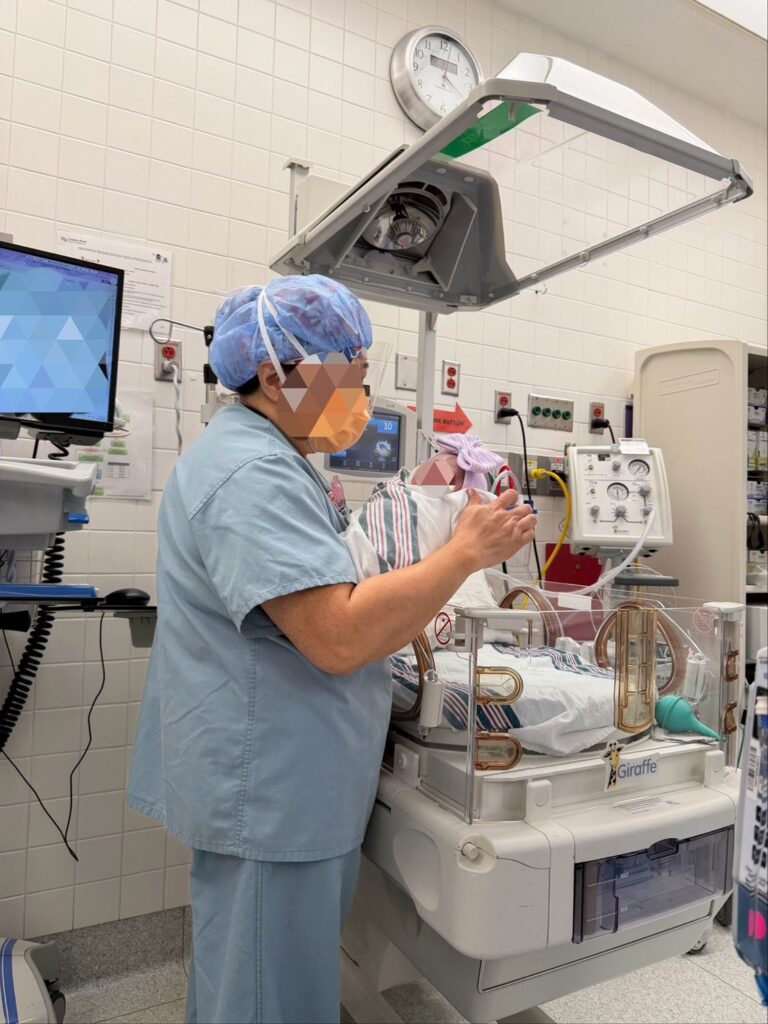 帝王切開で誕生し、手術室でスタッフに抱かれる新生児